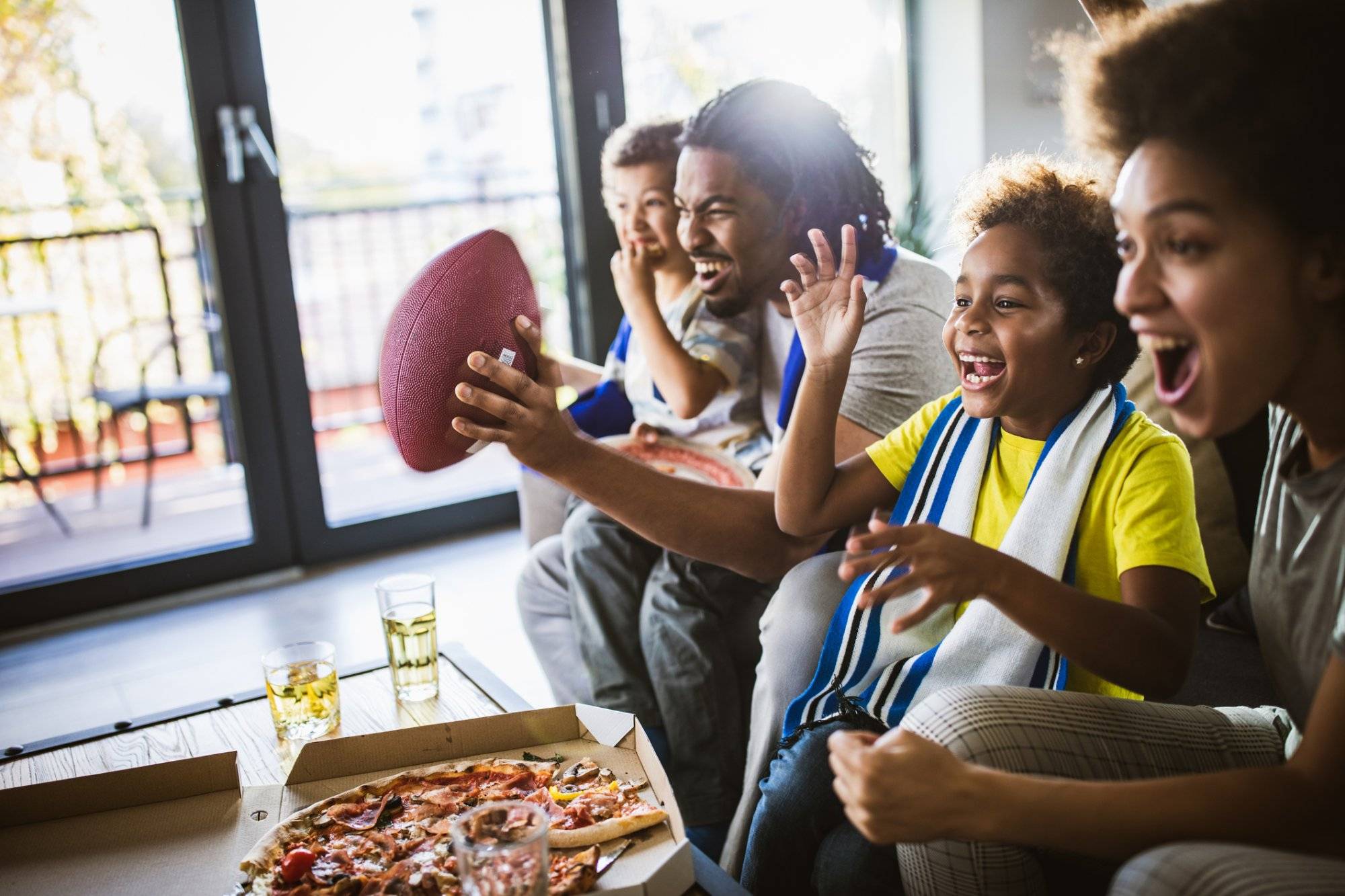 Cheerful black family cheering while watching rugby match on TV at home. Cheerful black family cheering while watching rugby match on TV at home.